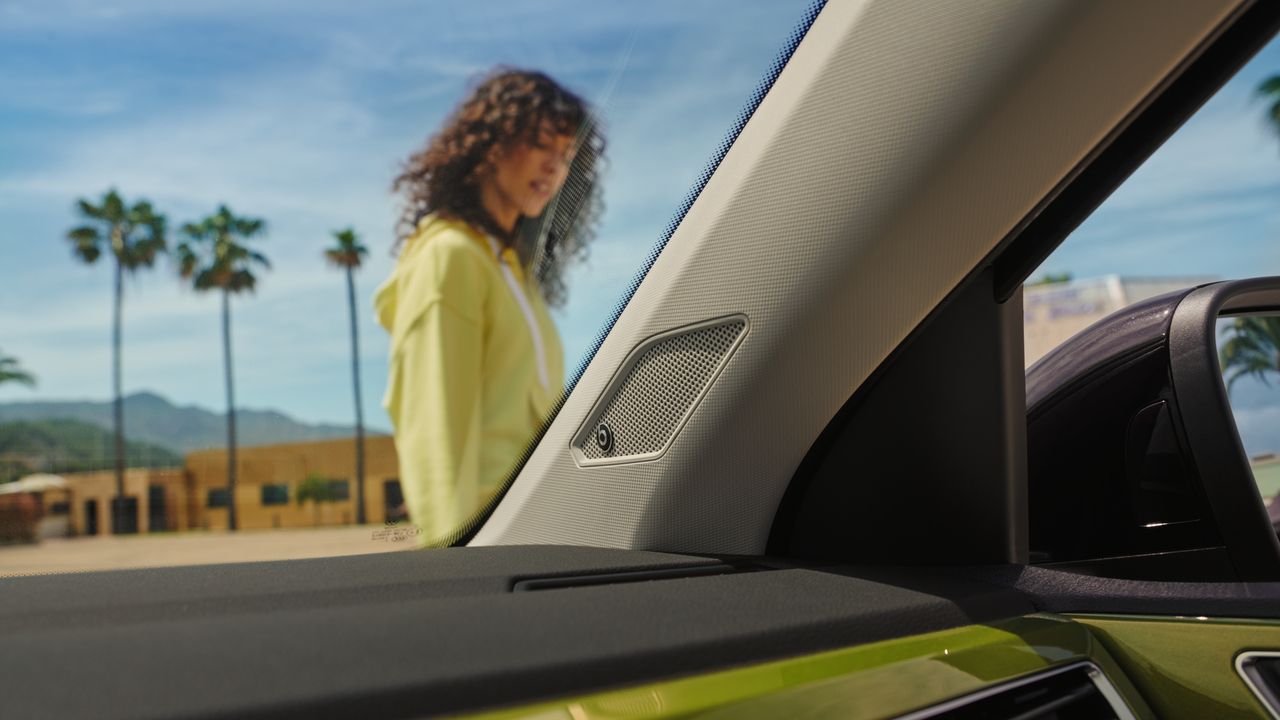 Vedere prin parbrizul unui VW Taigo asupra unei femei, cu difuzoarele sistemului de sonorizare opțional BeatsAudio™ în centru