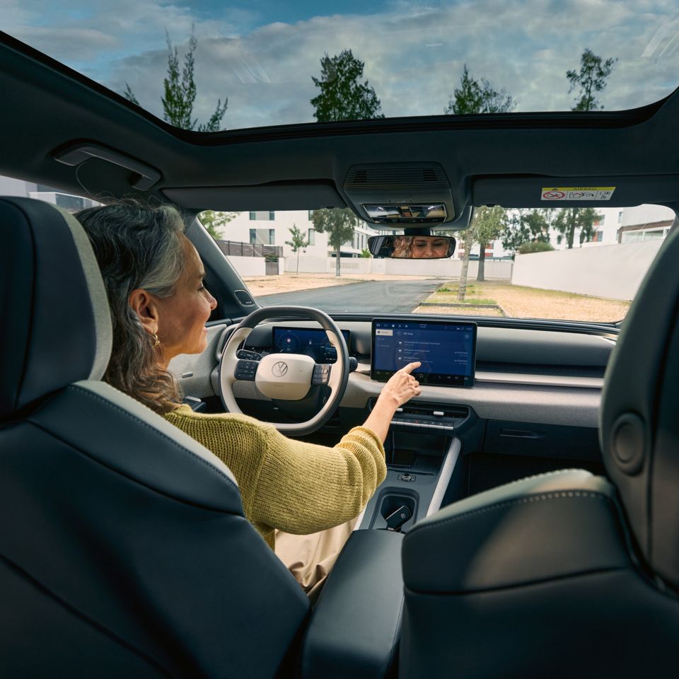 Eine Frau sitzt auf dem Fahrersitz eines VW ID. Cross und bedient das Infotainment-System.