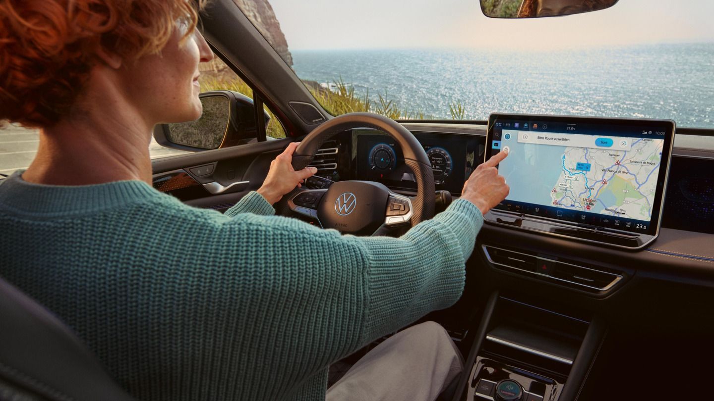  Eine Frau sitzt im VW Tiguan und bedienet das Infotainmentsystem mit Navigationsfunktion.