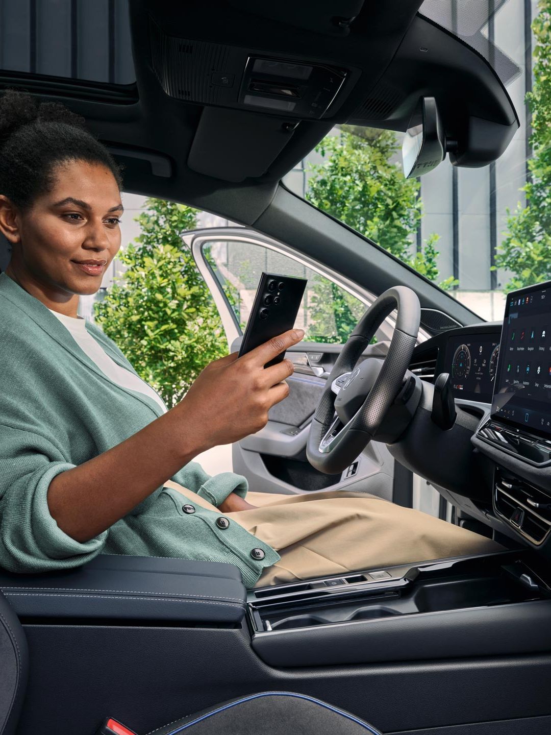 O femeie stă cu ușa deschisă pe scaunul șoferului unui VW Passat parcat și se uită la smartphone-ul său.
