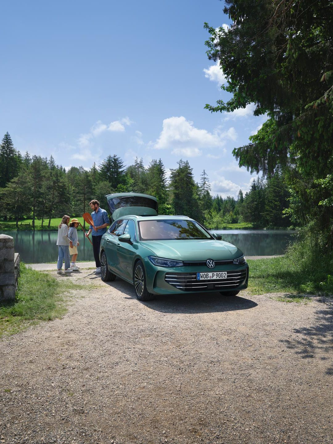 Un VW Passat verde albăstrui parcat lângă un ștrand, cu portbagajul deschis. Un bărbat le împarte jucării celor doi copii.