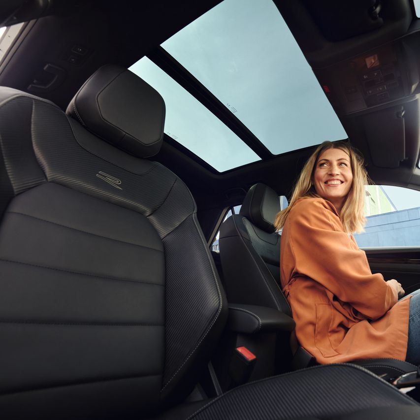 Frau sitzt in T-Roc R-Line mit Panoramadach und grinst