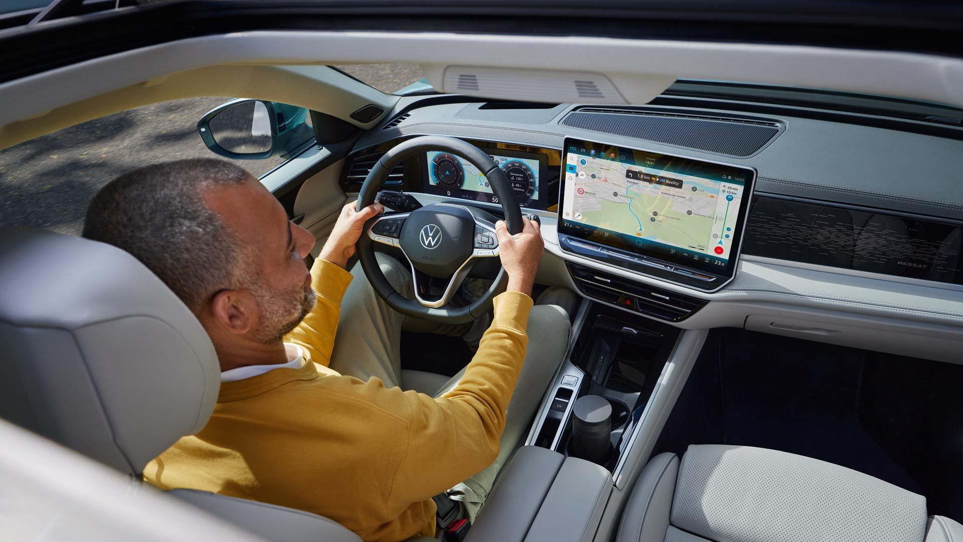 Vedere de sus prin trapa glisantă opțională deschisă a modelului VW Passat, în care un bărbat stă cu ambele mâini pe volan.