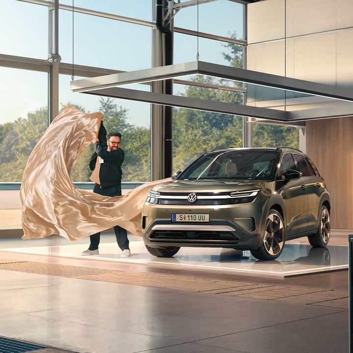 Ein Mann zieht ein großes Tuch von einem grünen VW ID. Cross, der in einem minimalistisch eingerichteten Designstudio steht.
