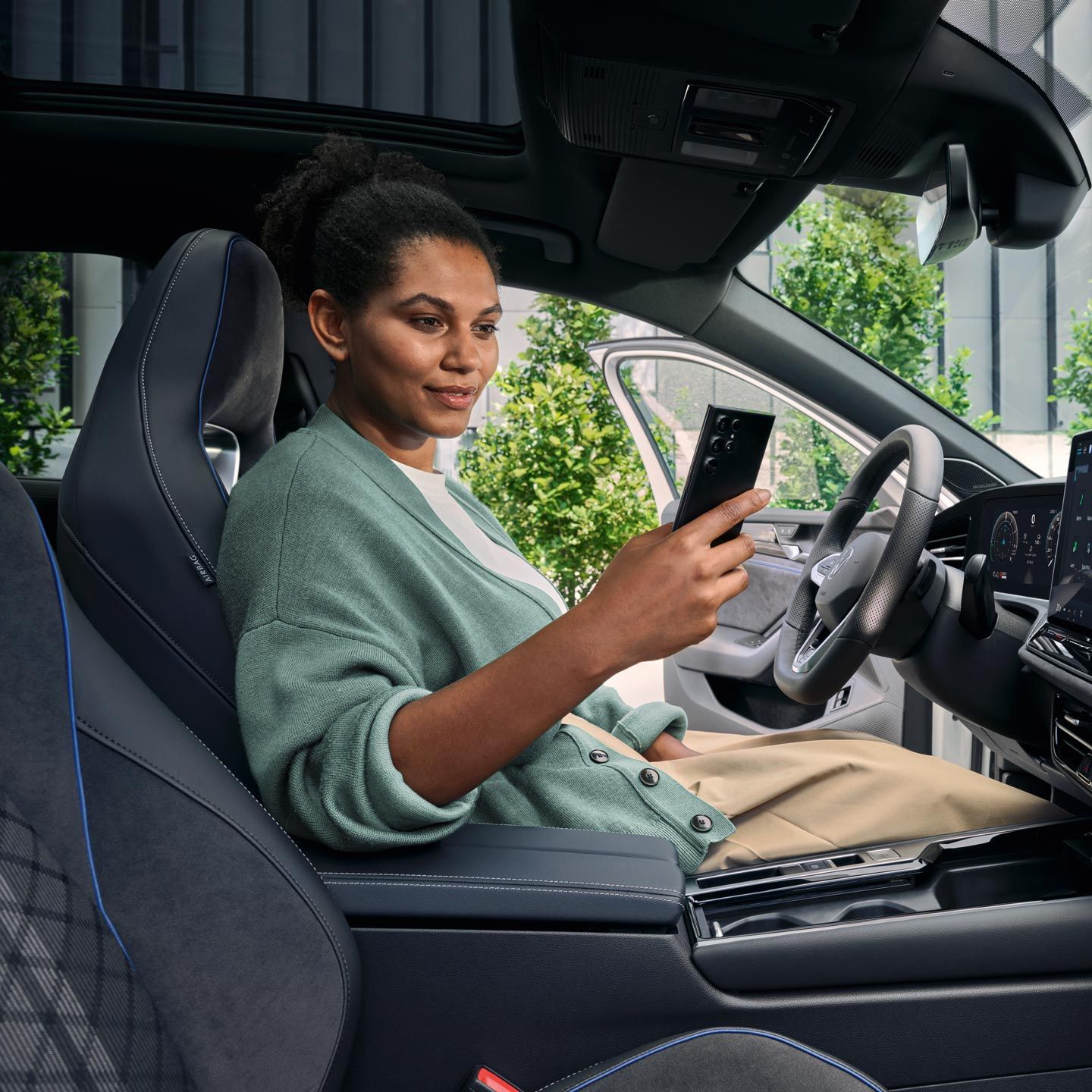 O femeie stă cu ușa deschisă pe scaunul șoferului unui VW Passat parcat și se uită la smartphone-ul său.