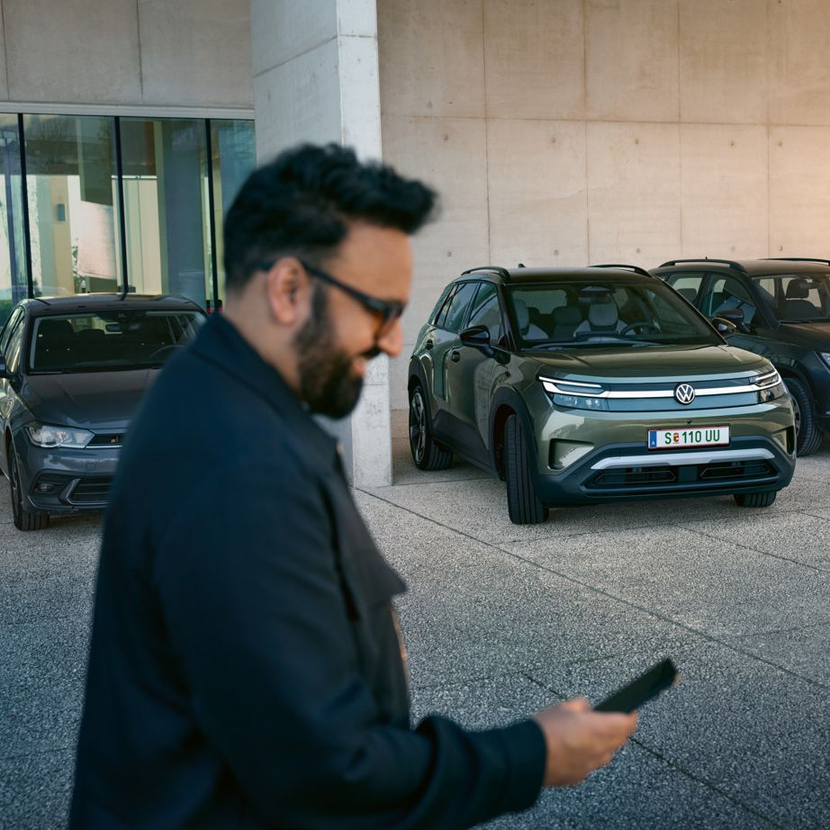 Ein Mann schaut auf sein Smartphone, im Hintergrund fährt ein VW ID. Cross automatisch in eine Parklücke.