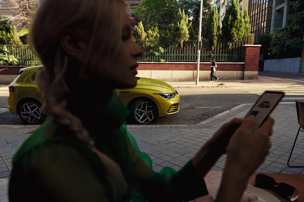 Eine Frau bedient ihr Smartphone, hinter ihr parkt ein VW Golf.