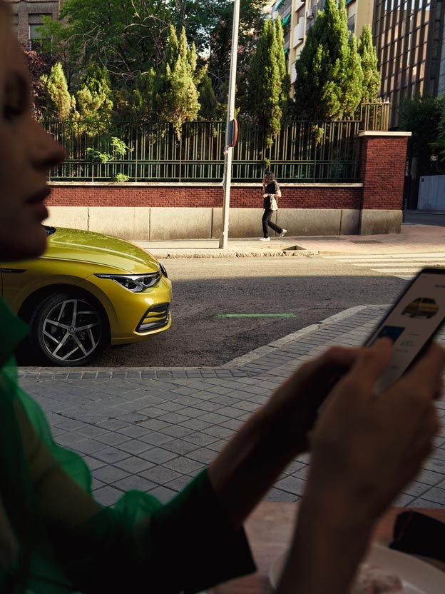 Eine Frau bedient ihr Smartphone, hinter ihr parkt ein VW Golf.