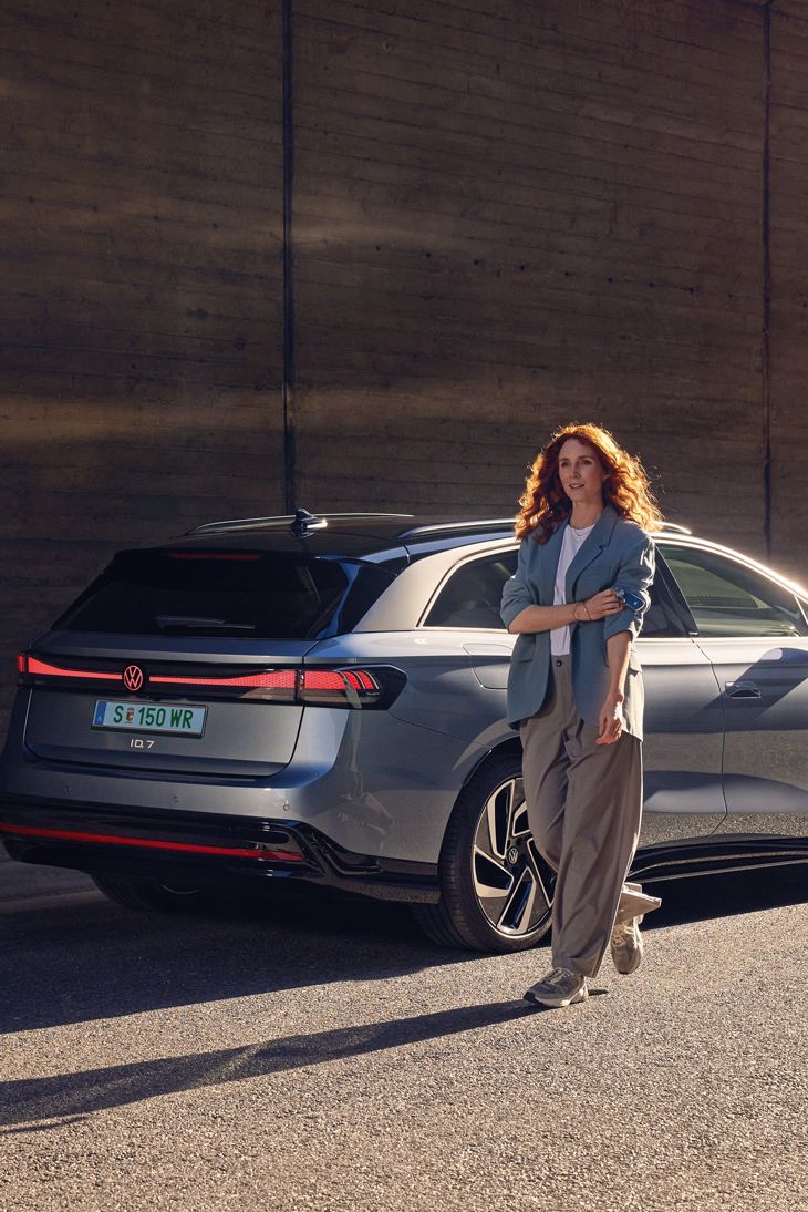 Eine Frau steht schräg vor dem Heck eines ID.7 Tourer
