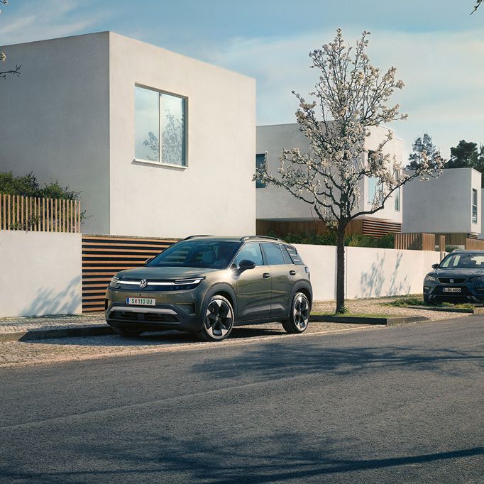 Ein grüner VW ID. Cross parkt in einer Parkbucht eines Wohngebiets mit blühenden Bäumen.