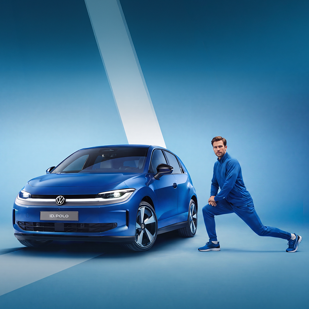 [AI-generated] – Automobil Volkswagen albastru, fotografiat din față și lateral, pe un fundal albastru. Lângă mașină, o persoană îmbrăcată în trening albastru execută o fandare. Pe partea frontală a automobilului este vizibil logo-ul Volkswagen și inscripția «ID.POLO».