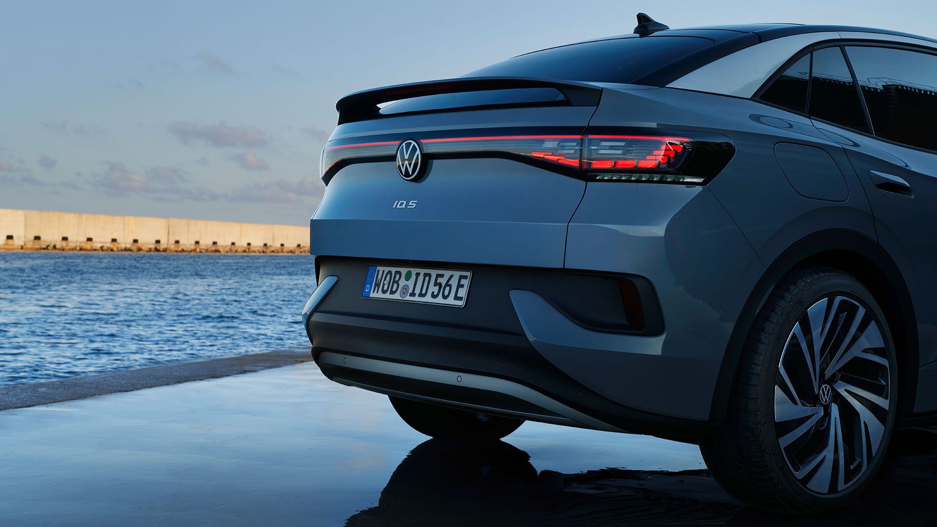 Partea din spate a unui VW ID.5 staționat, atmosferă de seară la mare, blocuri optice spate cu leduri aprinse