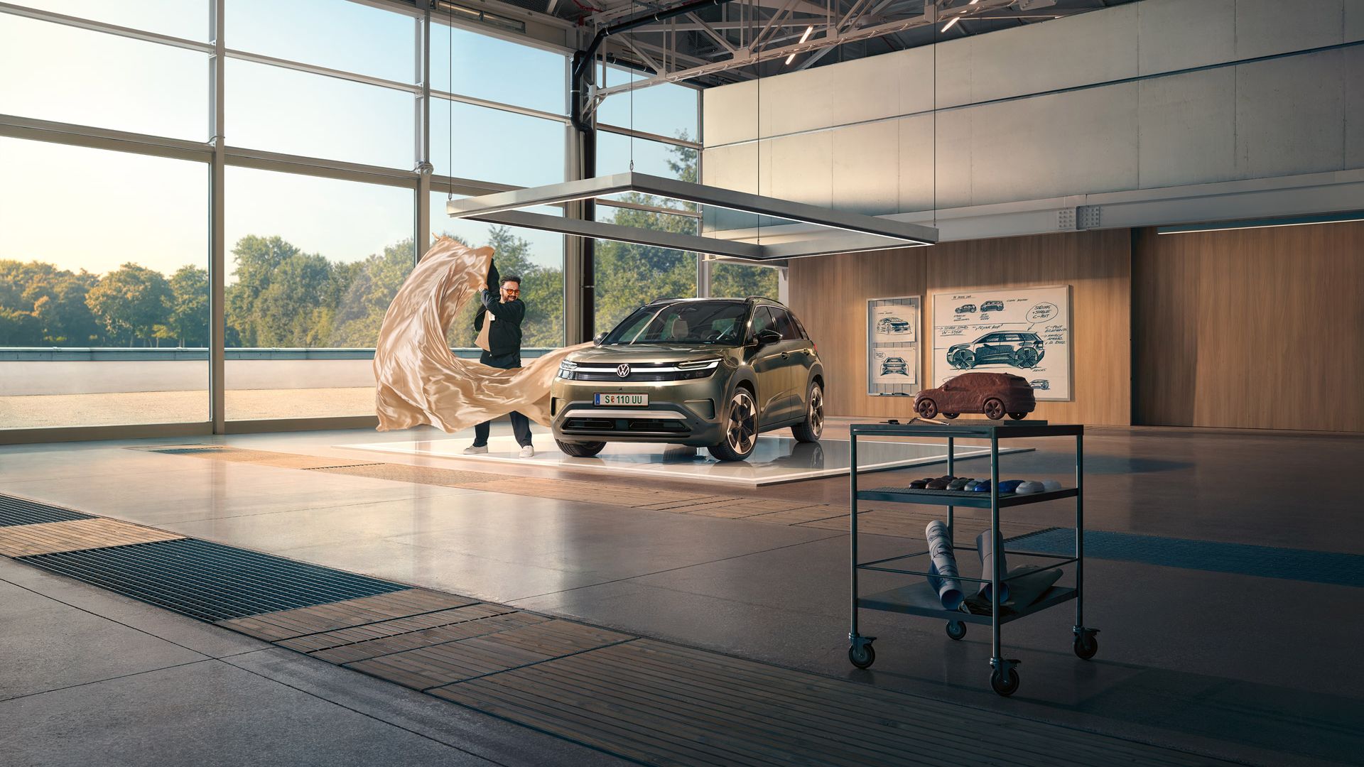Ein Mann zieht ein großes Tuch von einem grünen VW ID. Cross, der in einem minimalistisch eingerichteten Designstudio steht.