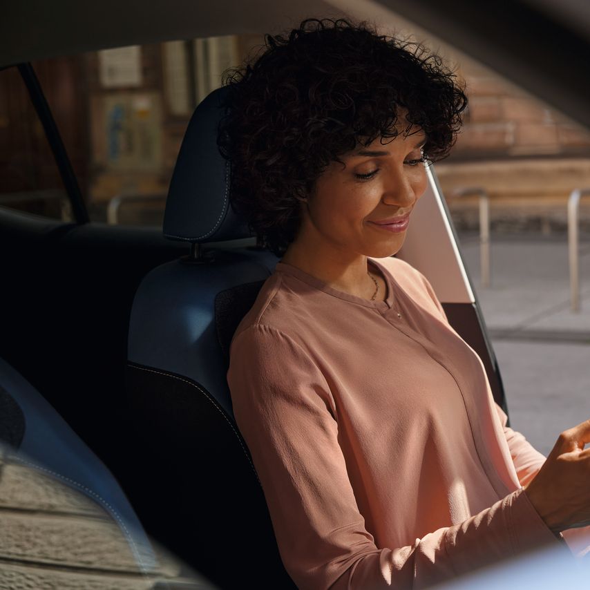 O femeie zâmbitoare aflată pe scaunul șoferului unui VW T-Cross parcat își privește telefonul mobil.