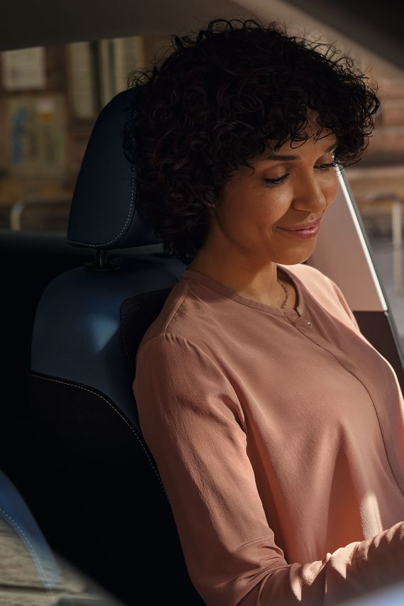 O femeie zâmbitoare aflată pe scaunul șoferului unui VW T-Cross parcat își privește telefonul mobil.