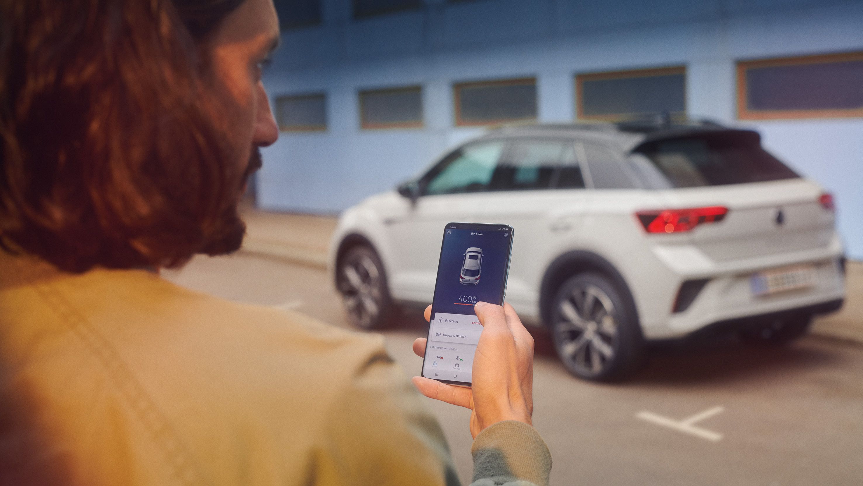 VW T-Roc R-Line de culoare albă în fața unei clădiri, este vizibil lateralul, un bărbat cu un smartphone în prim plan