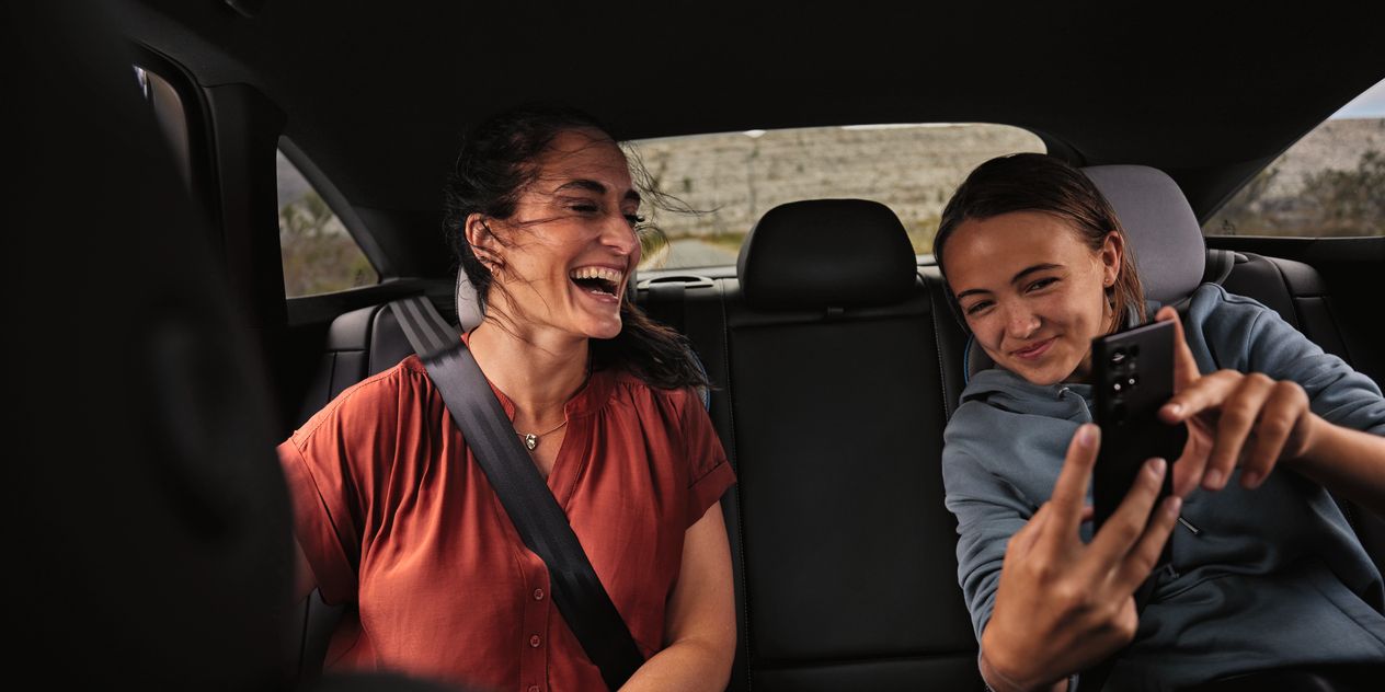 Zwei Frauen sitzen auf Rückbank und lachen über Inhalt im Smartphone