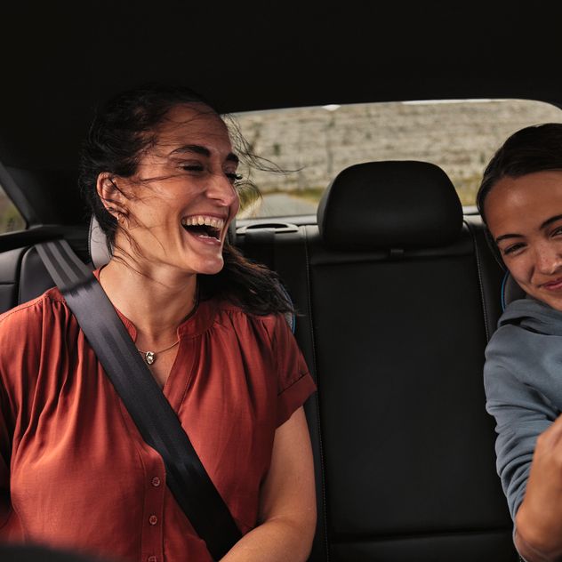 Zwei Frauen sitzen auf Rückbank und lachen über Inhalt im Smartphone