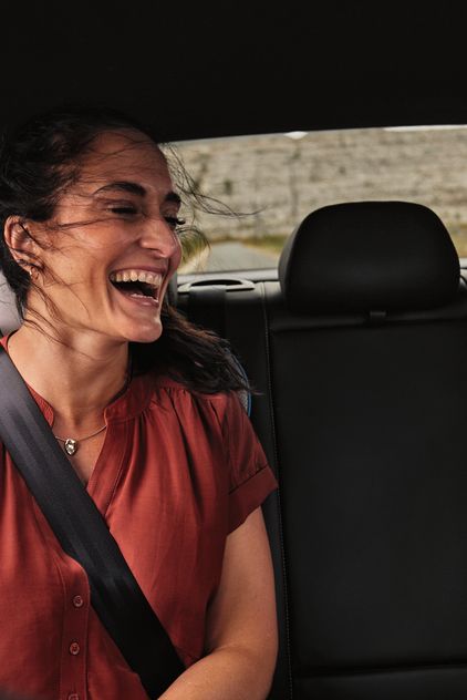 Zwei Frauen sitzen auf Rückbank und lachen über Inhalt im Smartphone