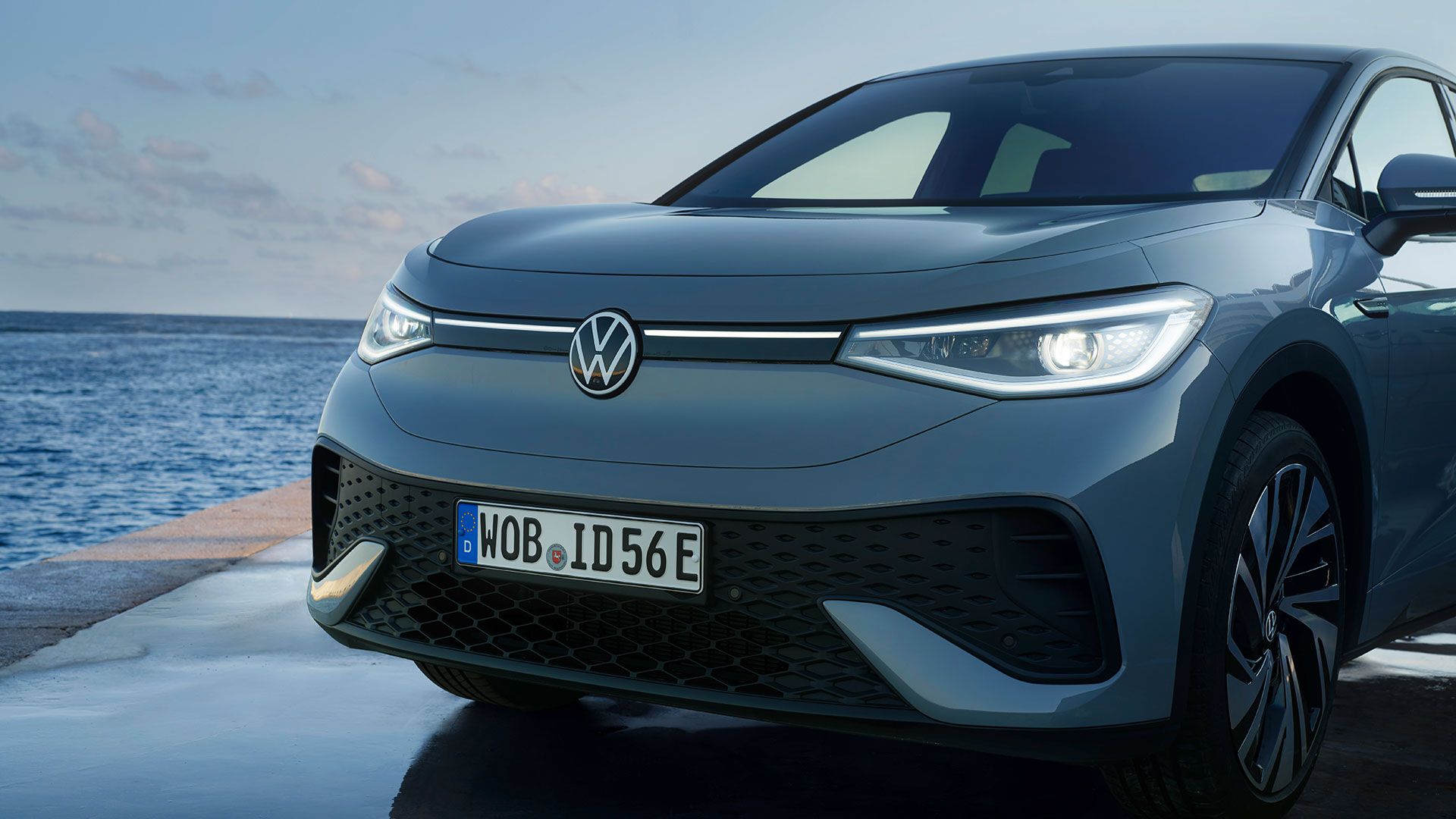 Partea din față a unui VW ID.5 staționat pe cheiul unui port în lumina serii, farurile cu leduri aprinse
