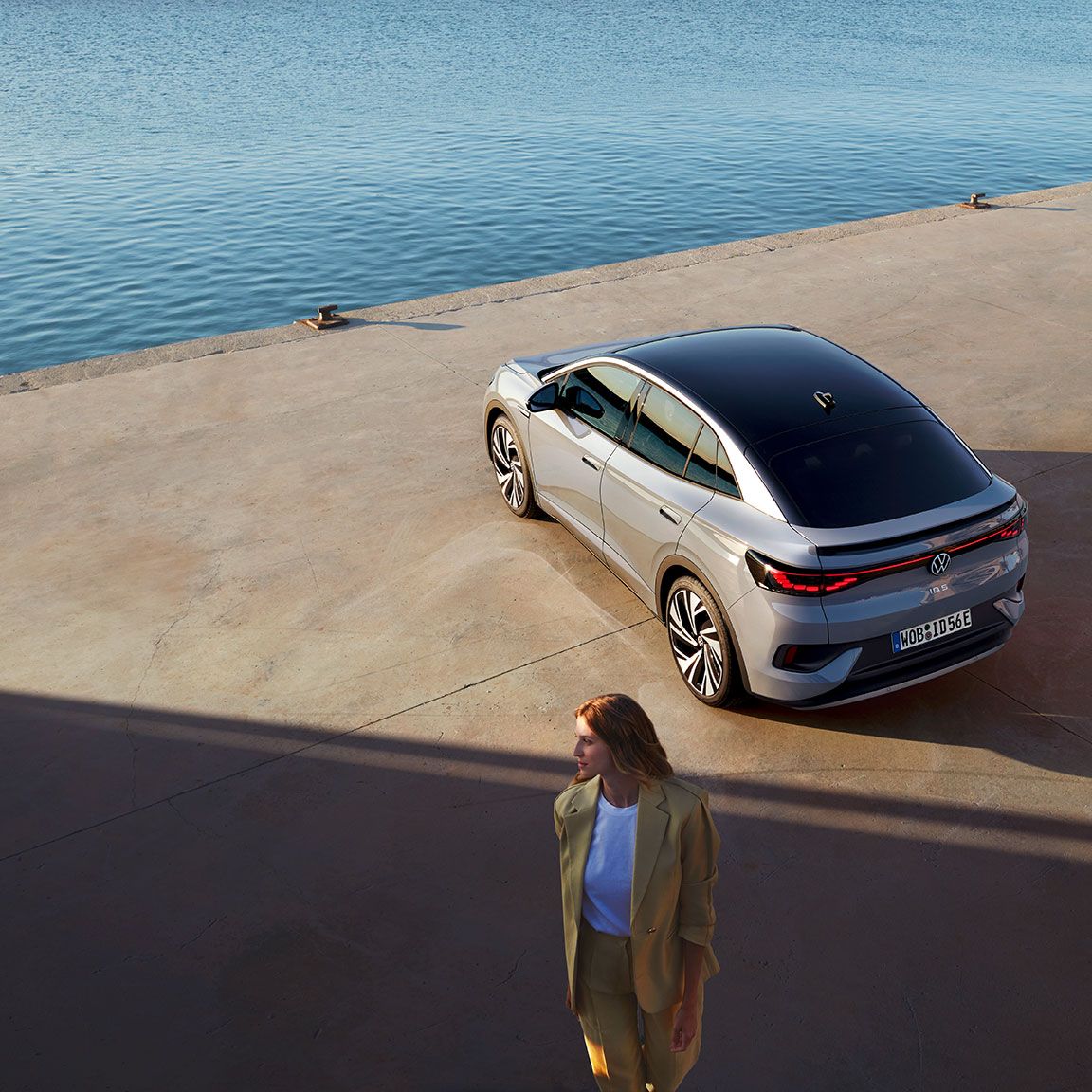 Heckansicht eines VW ID.5 an einem Hafenkai, Blick von schräg oben, im Vordergrund steht eine Frau