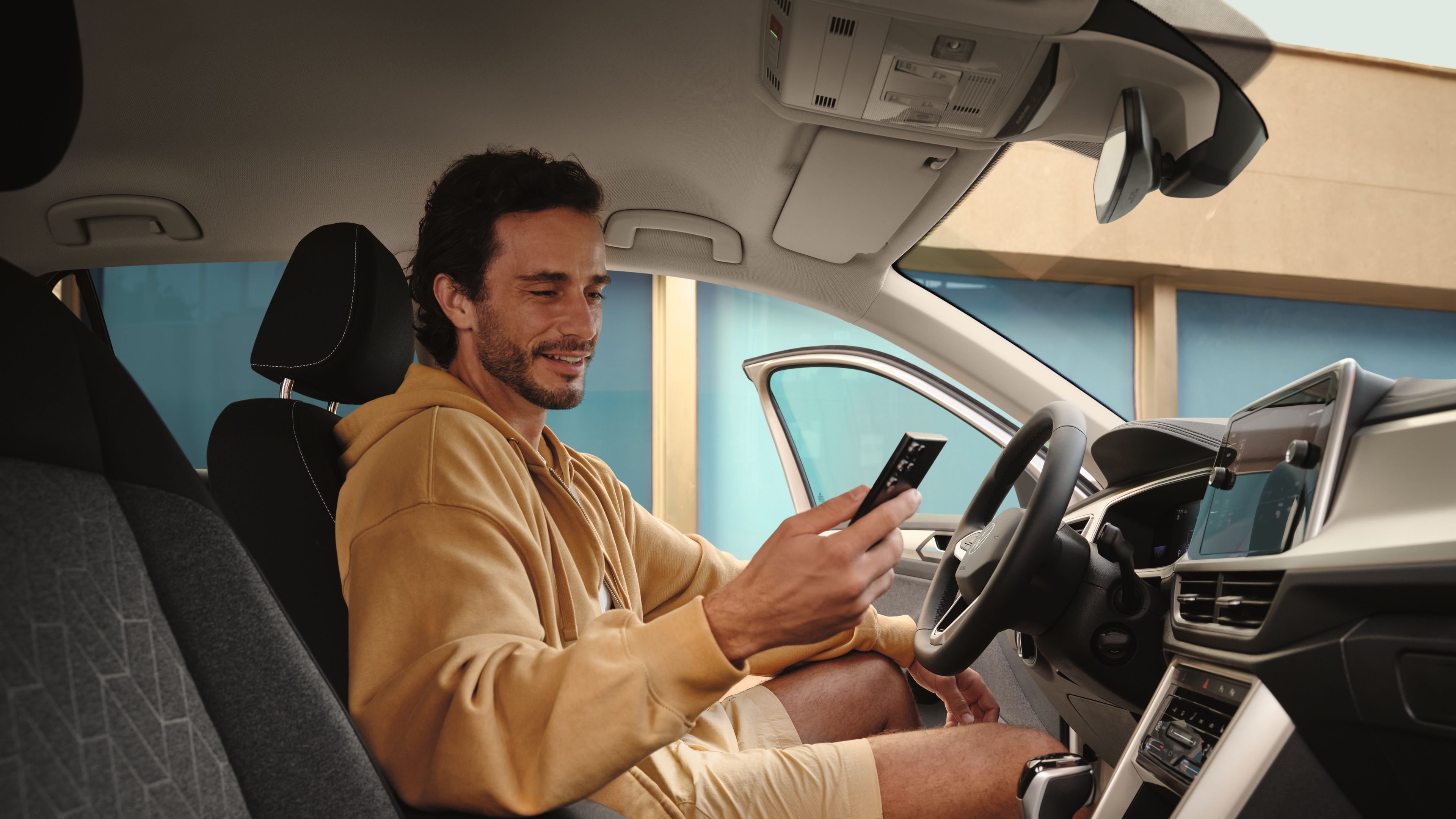 Mann sitzt in VW T-Roc und blickt auf Smartphone