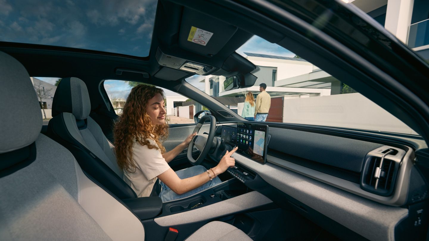 Eine junge Frau sitzt auf dem Fahrersitz eines VW ID. Cross und bedient das Infotainment-System.