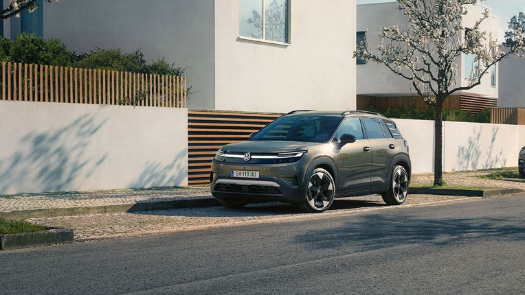 Ein grüner VW ID. Cross parkt in einer Parkbucht eines Wohngebiets mit blühenden Bäumen.