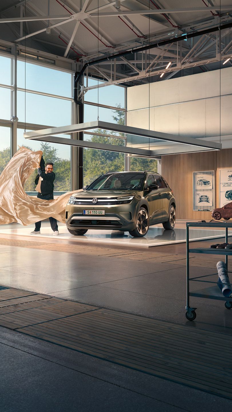 Ein Mann zieht ein großes Tuch von einem grünen VW ID. Cross, der in einem minimalistisch eingerichteten Designstudio steht.