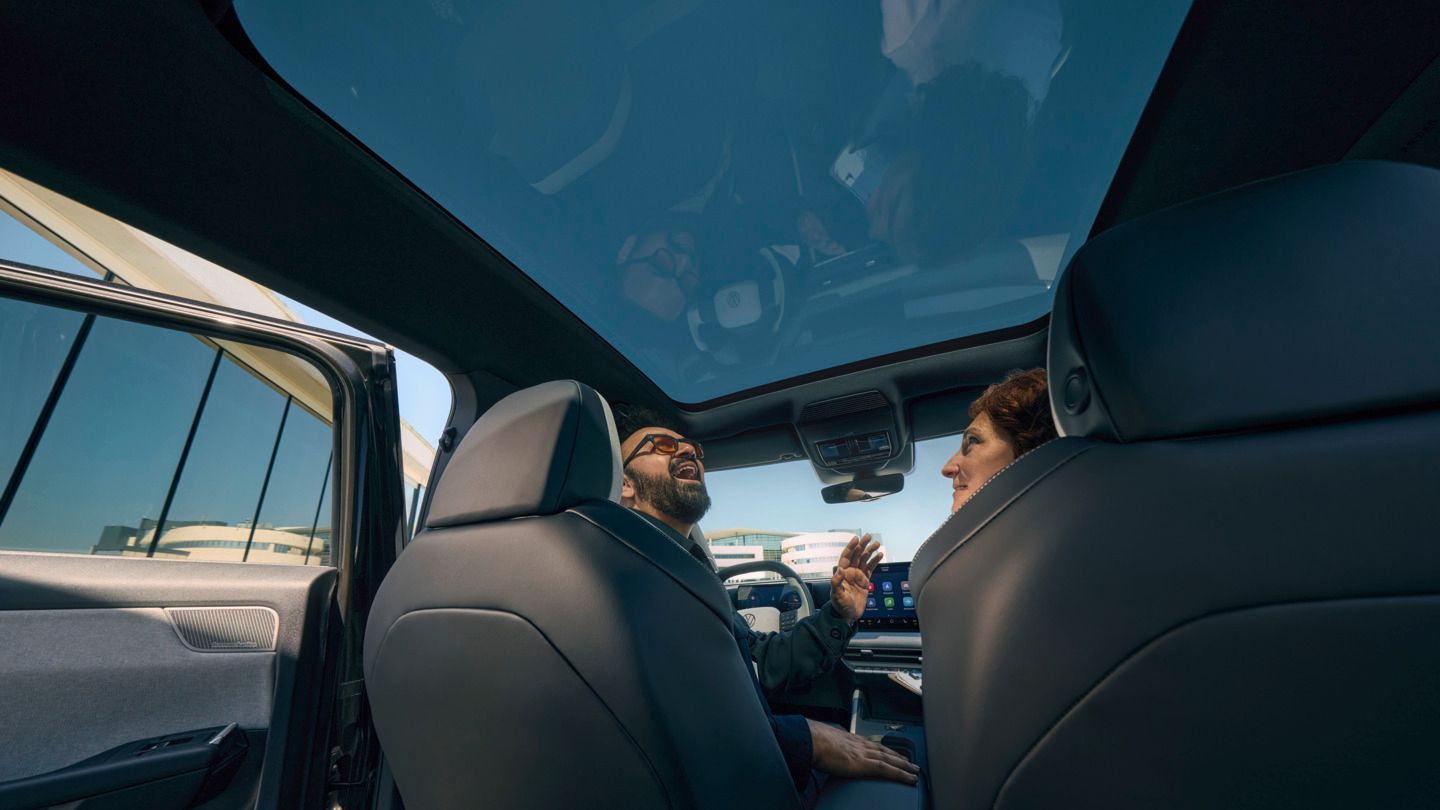 Ein Mann sitzt lachend auf dem Fahrersitz eines VW ID. Cross und schaut durch das geöffnete Panoramadach, eine Frau sitzt auf dem Beifahrersitz.