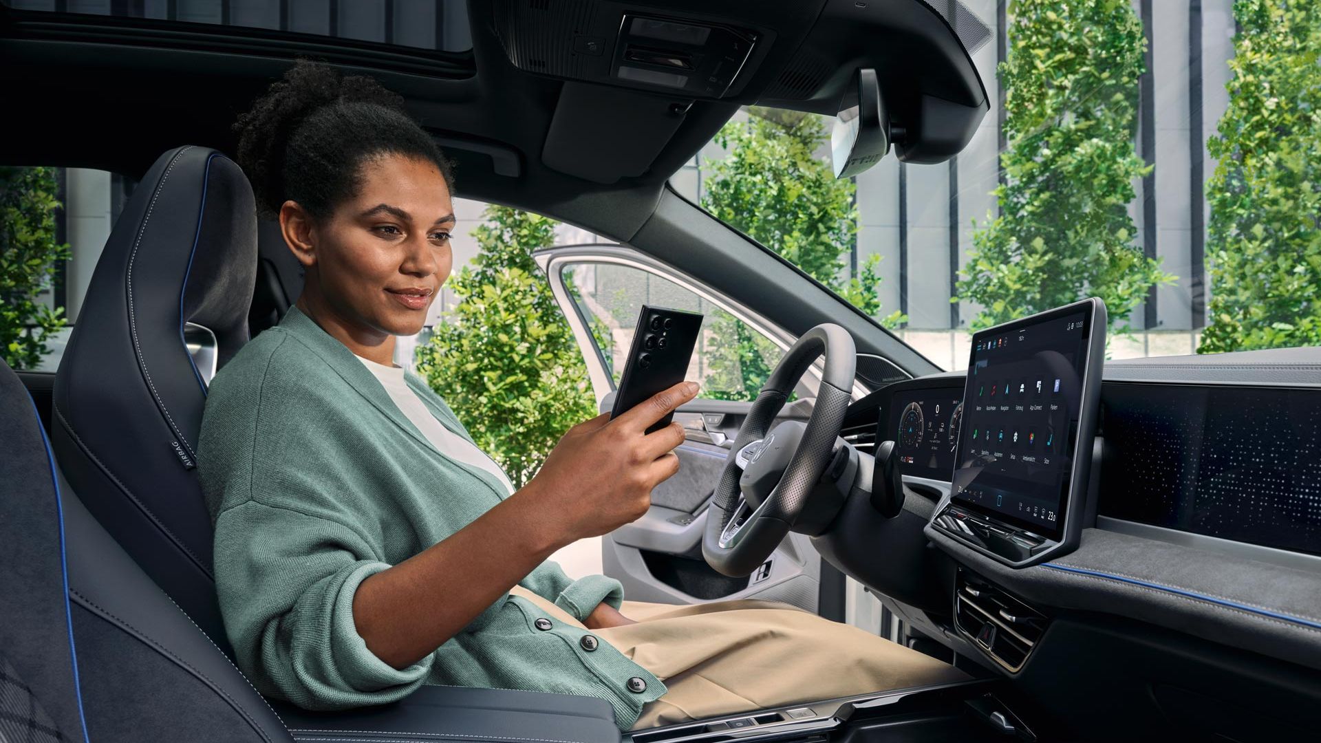 O femeie stă cu ușa deschisă pe scaunul șoferului unui VW Passat parcat și se uită la smartphone-ul său.