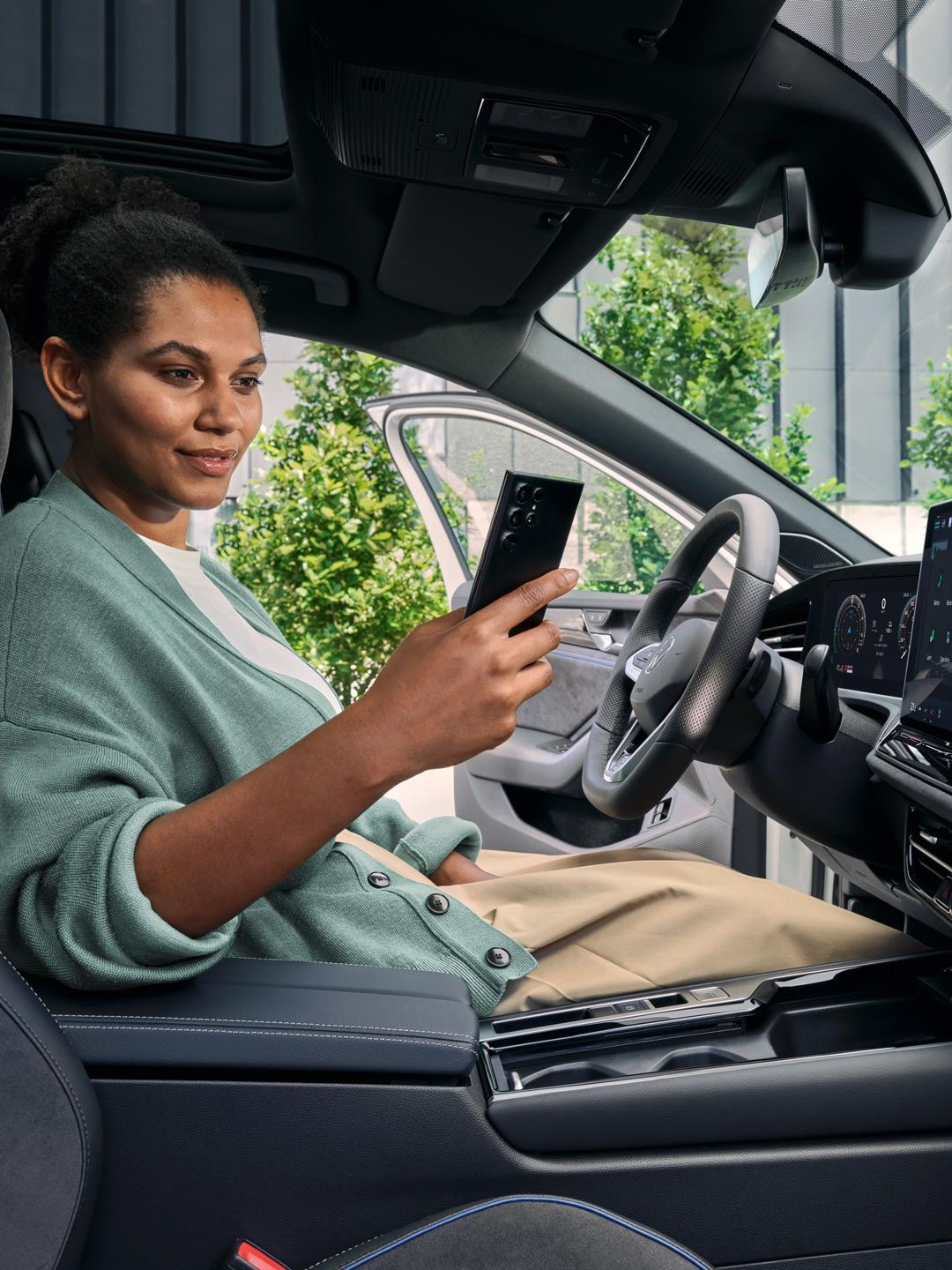 O femeie stă cu ușa deschisă pe scaunul șoferului unui VW Passat parcat și se uită la smartphone-ul său.
