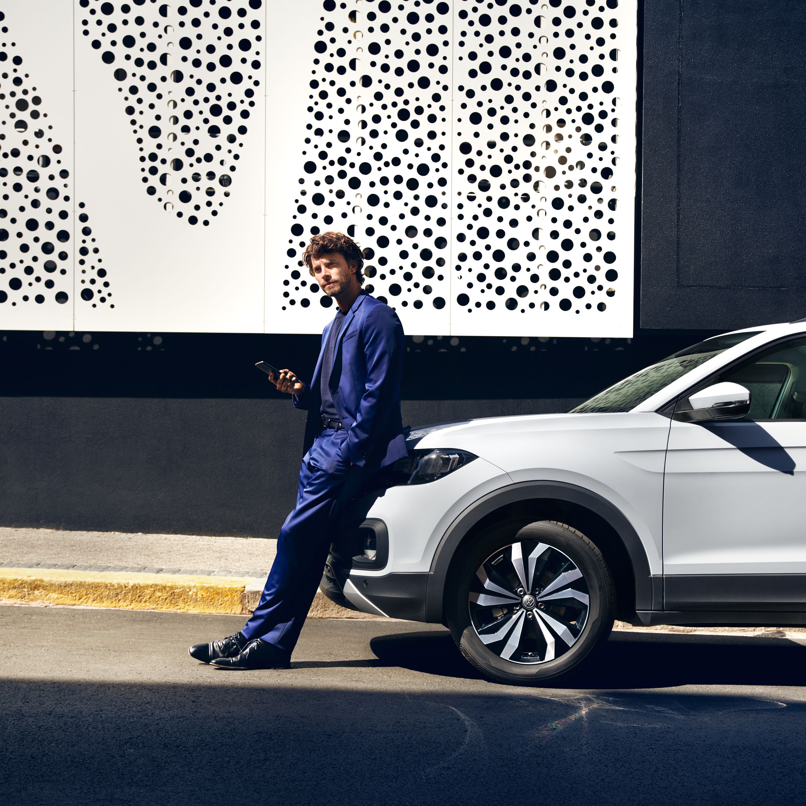 Mann lehnt an VW T-Cross mit Smartphone in der Hand und liest Newsletter