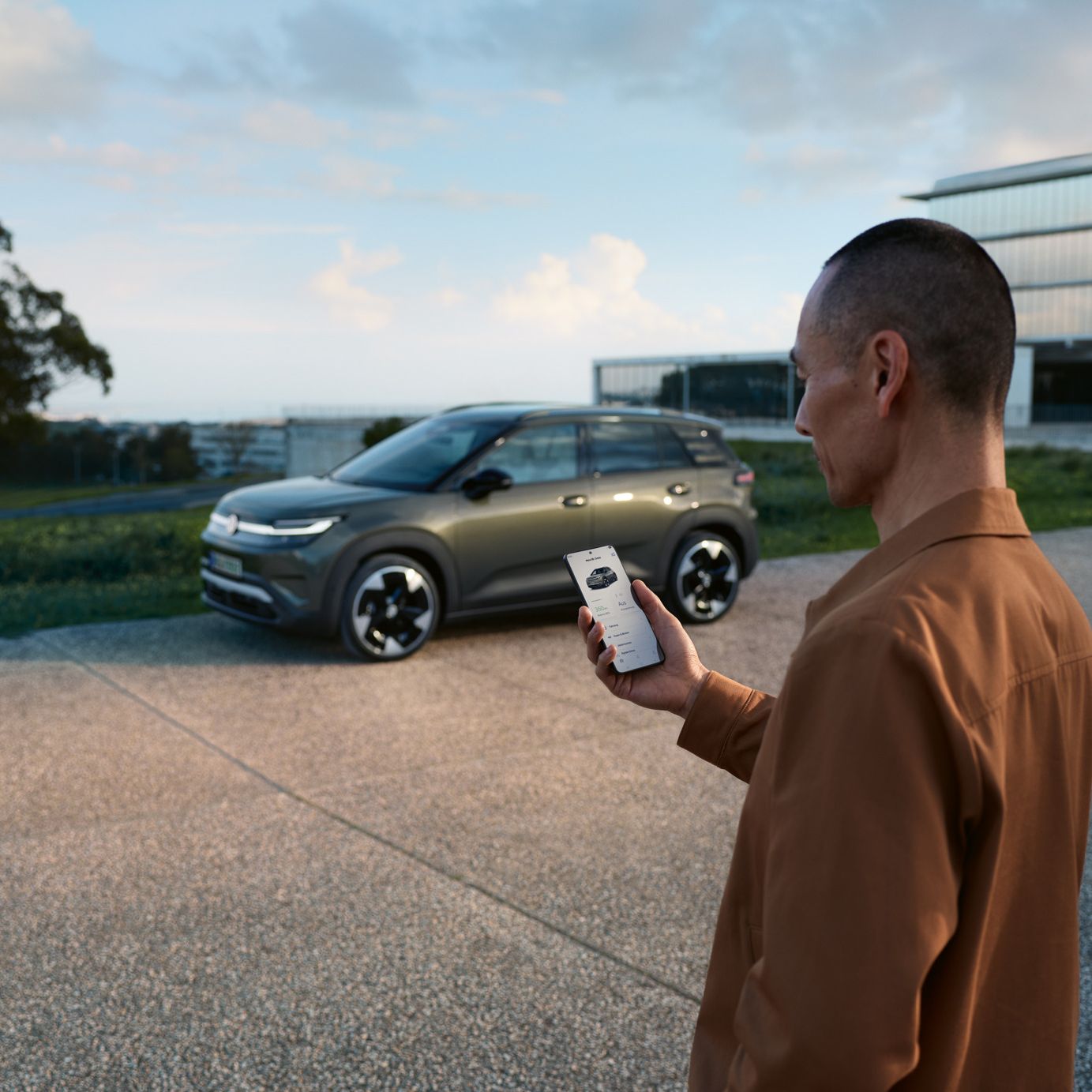Ein grüner VW ID.Cross parkt an einem Wohnhaus, daneben steht ein Mann und schaut auf sein Smartphone.