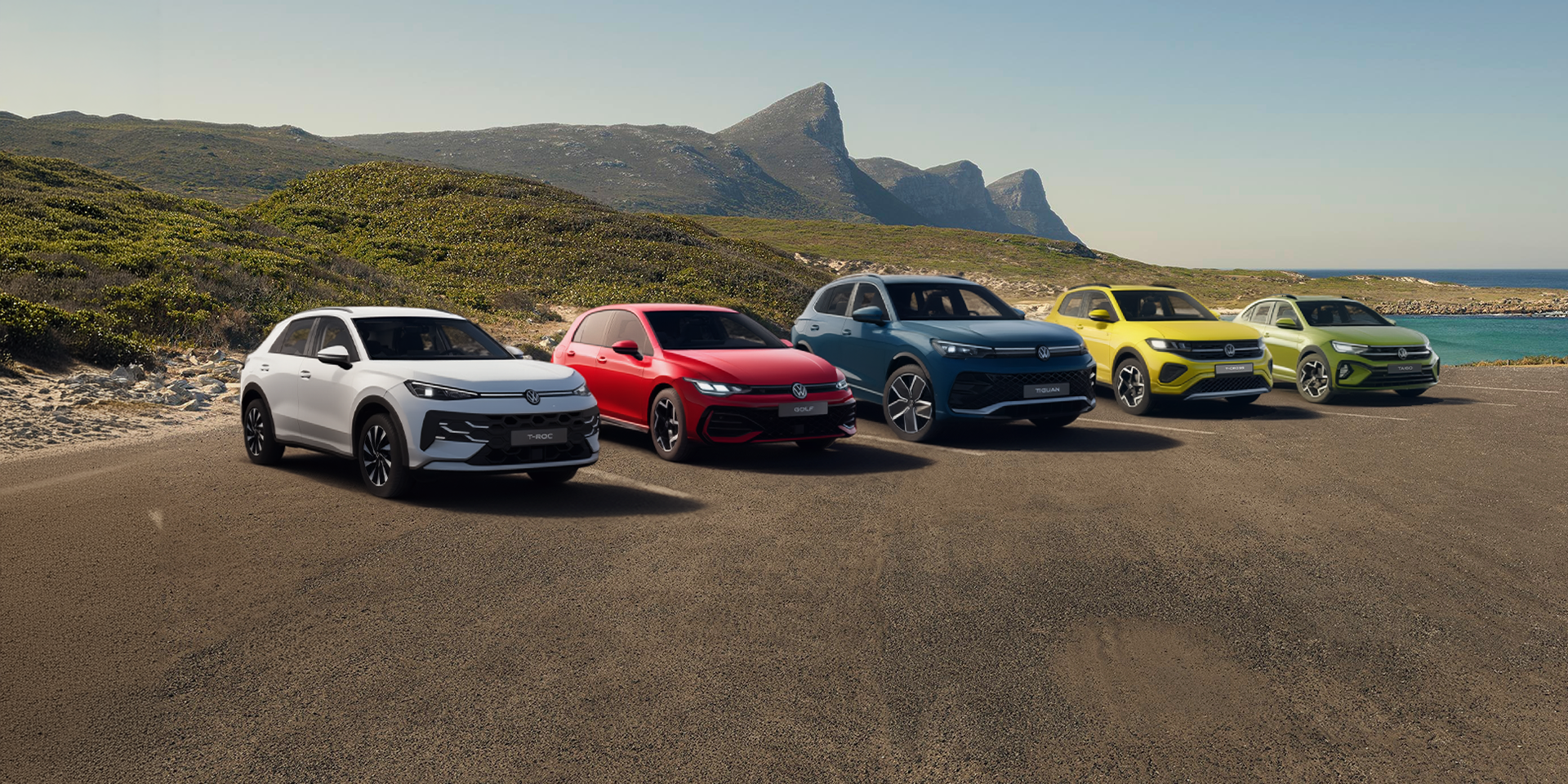Mai multe modele Volkswagen hibrid (T-Roc, Golf, Tiguan, T-Cross si Taigo) afișate aliniat pe o șosea de coastă.