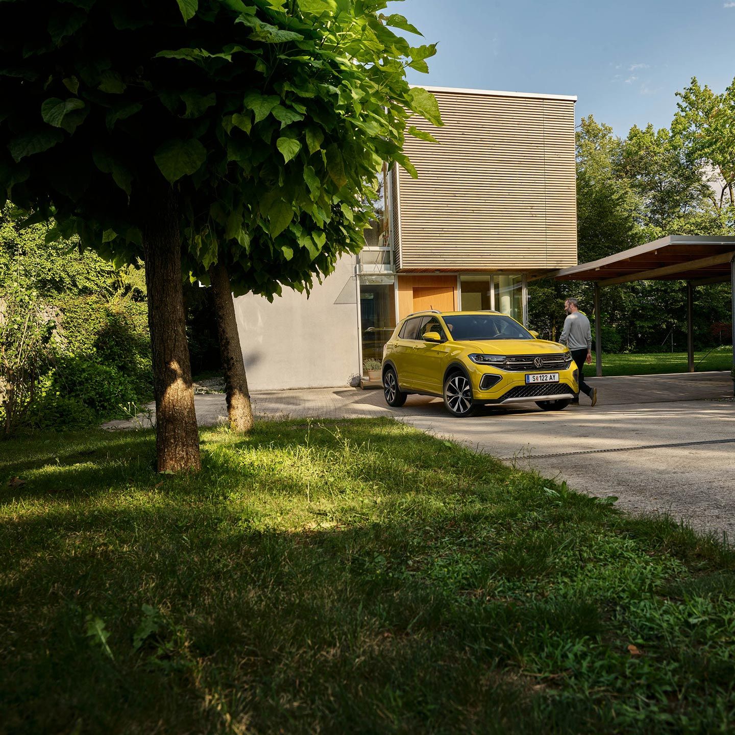 Un bărbat se pregătește să urce în noul VW T-Cross, care se află parcat văzut din față pe aleea de intrare din fața unei case.