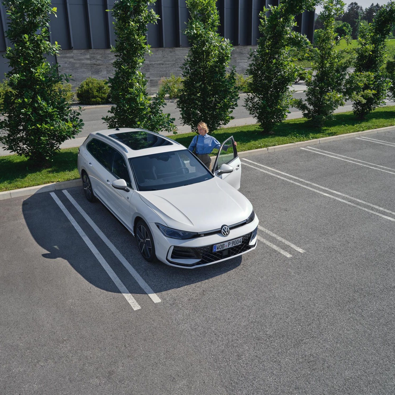 Vedere de sus a unui VW Passat într-o parcare, o femeie se urcă pe partea șoferului.