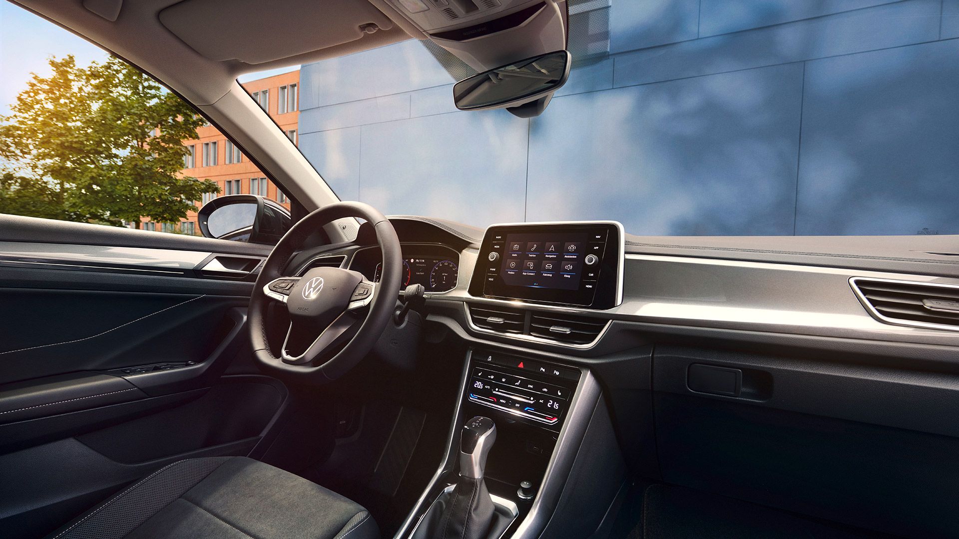 Interior VW T-Roc, perspectivă dinspre scaunul pasagerului față spre scaunul șoferului și postul de conducere cu volanul multifuncțional și sistemul Infotainment