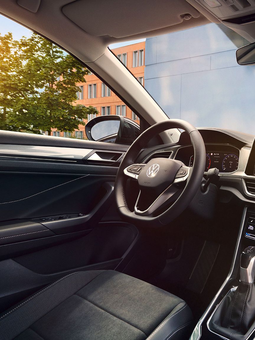 Interior VW T-Roc, perspectivă dinspre scaunul pasagerului față spre scaunul șoferului și postul de conducere cu volanul multifuncțional și sistemul Infotainment