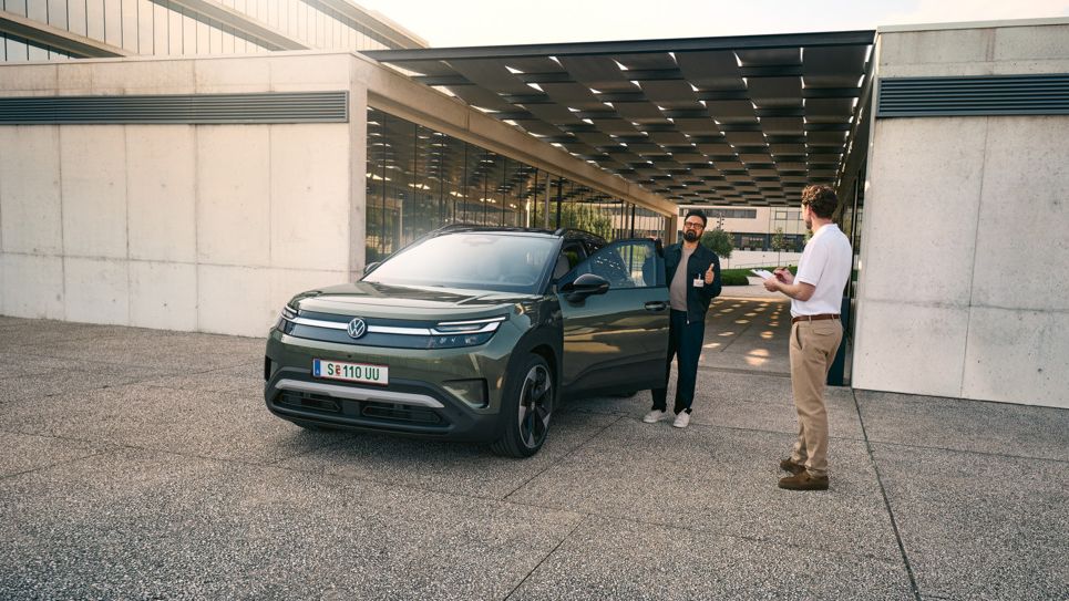 Ein Mann steigt in einen VW ID. Cross ein und unterhält sich dabei mit einem Ingenieur mit einem Klemmbrett in der Hand.
