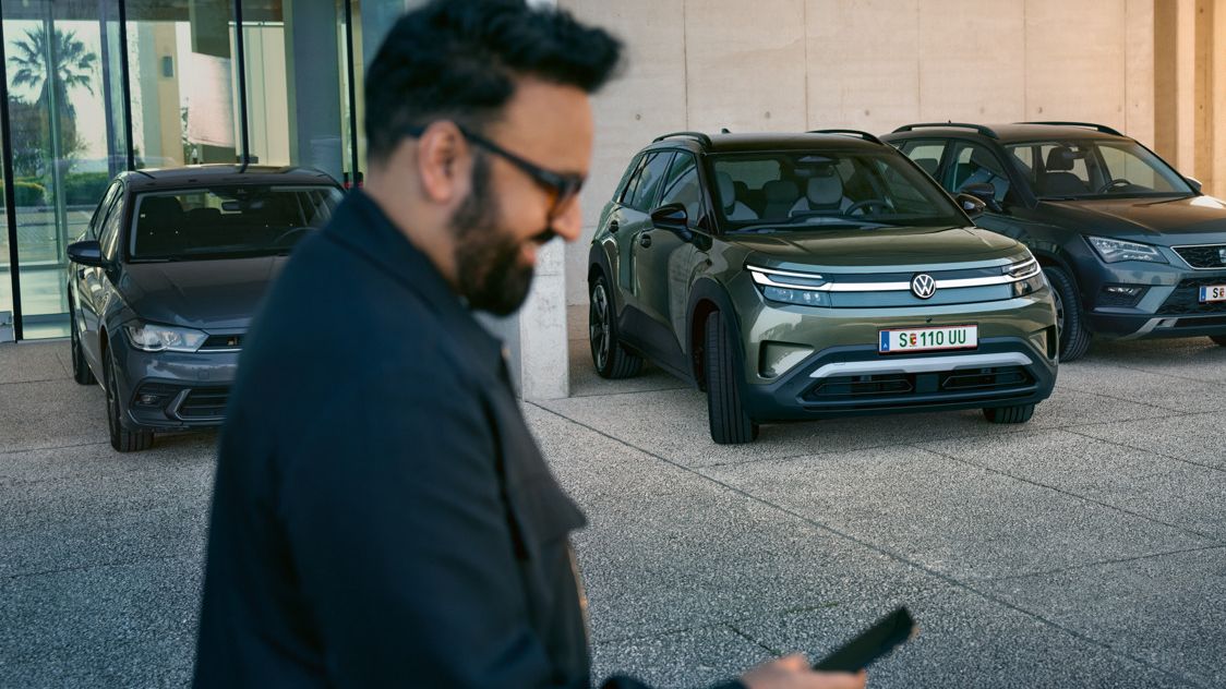 Ein Mann schaut auf sein Smartphone, im Hintergrund fährt ein VW ID. Cross automatisch in eine Parklücke.
