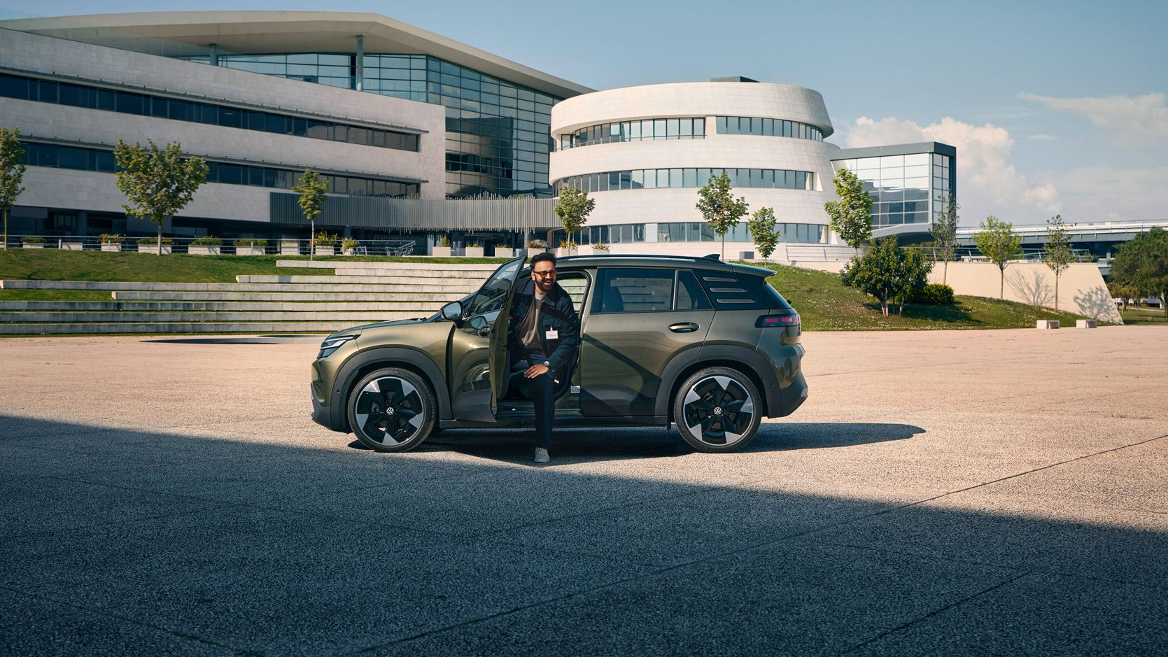 Ein Mann steigt aus der Fahrertür eines VW ID. Cross, der vor einem modernen, mehrstöckigen Firmengebäude steht.