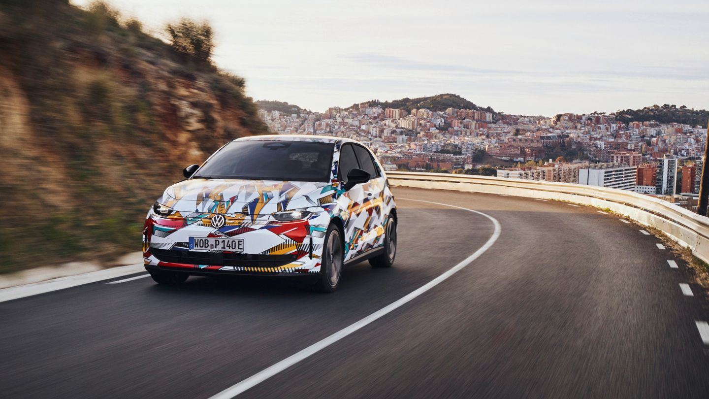 Un ID. Polo cu o vopsea colorată merge pe un drum șerpuit. În fundal se află un oraș cu multe case pe un deal. Drumul șerpuiește de-a lungul dealurilor.