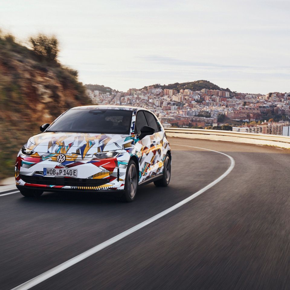 Un ID. Polo cu o vopsea colorată merge pe un drum șerpuit. În fundal se află un oraș cu multe case pe un deal. Drumul șerpuiește de-a lungul dealurilor.